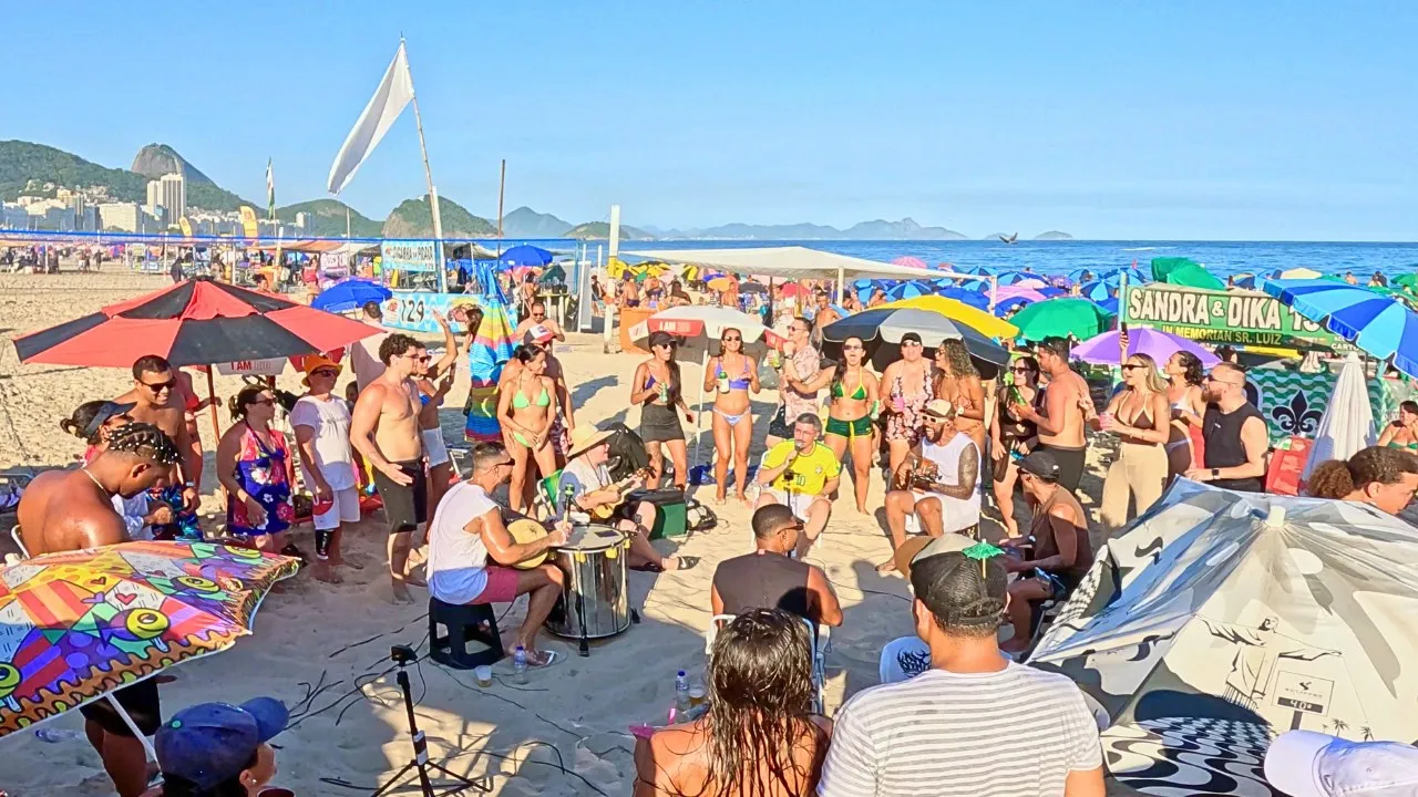 Vista panorâmica da praia de Copacabana lotada, com a roda de pagode em primeiro plano